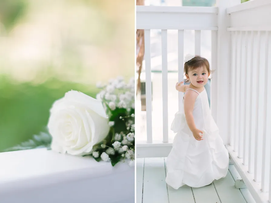 A toddler girl in a white dress standing by a white fence.